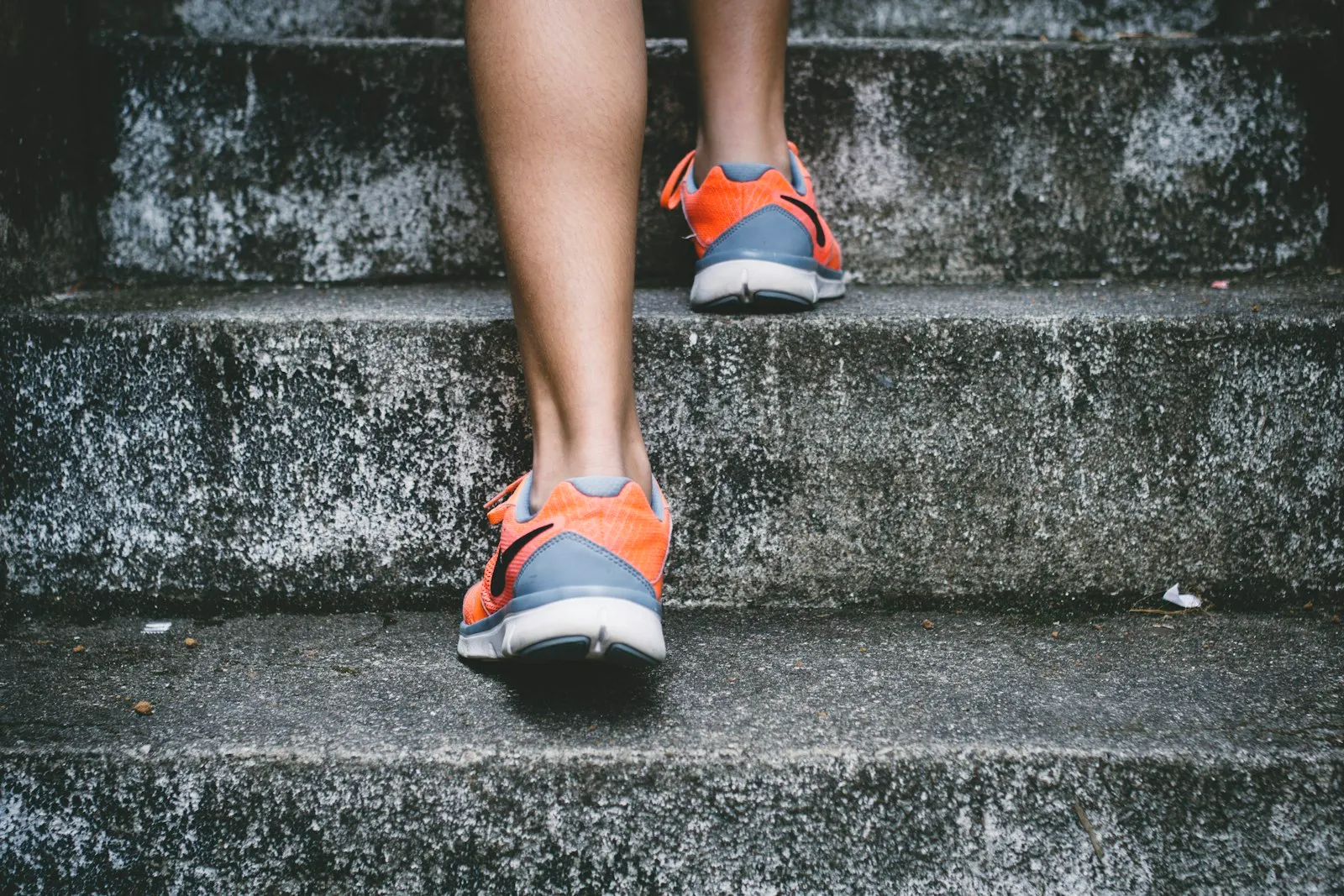 Osoba w pomarańczowych butach do biegania wbiegająca po schodach
